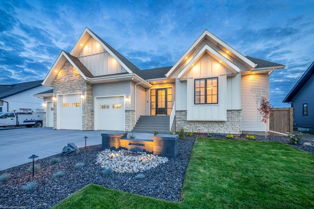 Front of a home at dusk with planted beds, river rock and a lit firepit