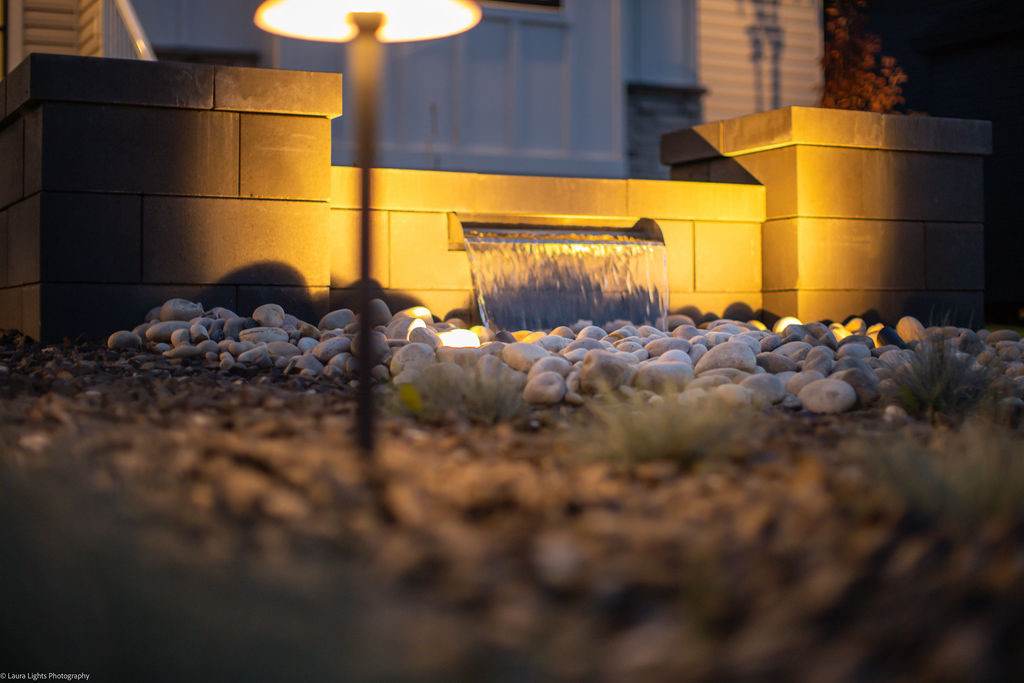 Close view of a lit sheer descent water feature spilling onto white river rock at night